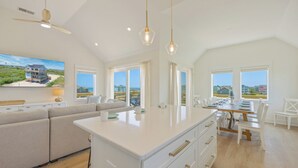 A spacious kitchen with a central island, large windows offering views of the beach, and a ceiling fan. - Oceanside Home in Rodanthe with Hot Tub, EV Charging, and Media Rooms (Rodanthe)