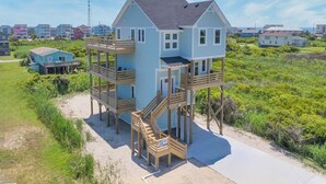 A two-story house with a wooden deck and a staircase leading to the upper floor. - Oceanside Home in Rodanthe with Hot Tub, EV Charging, and Media Rooms (Rodanthe)