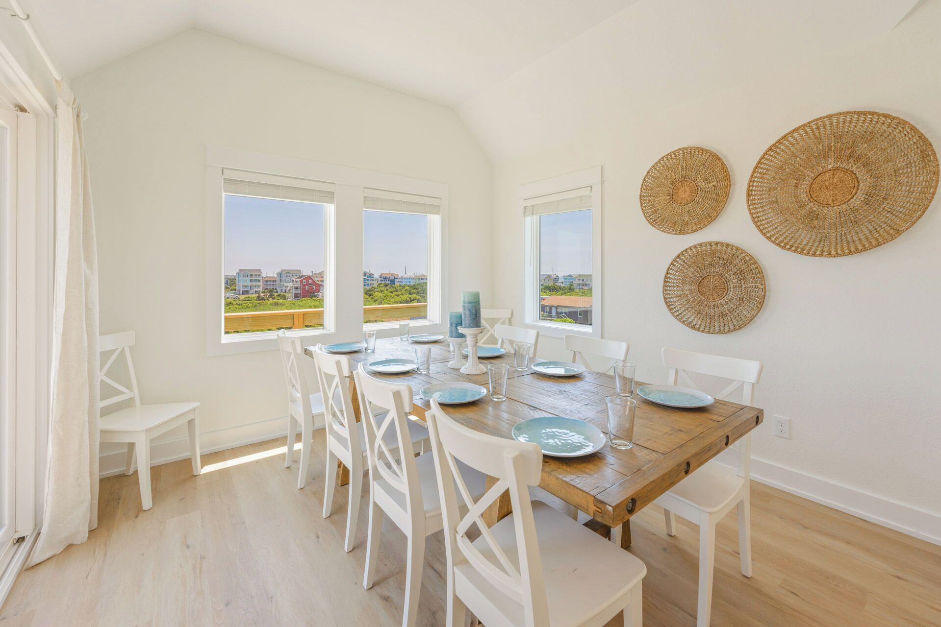 A dining area with a wooden table set for six, white chairs, and three woven wall decorations.