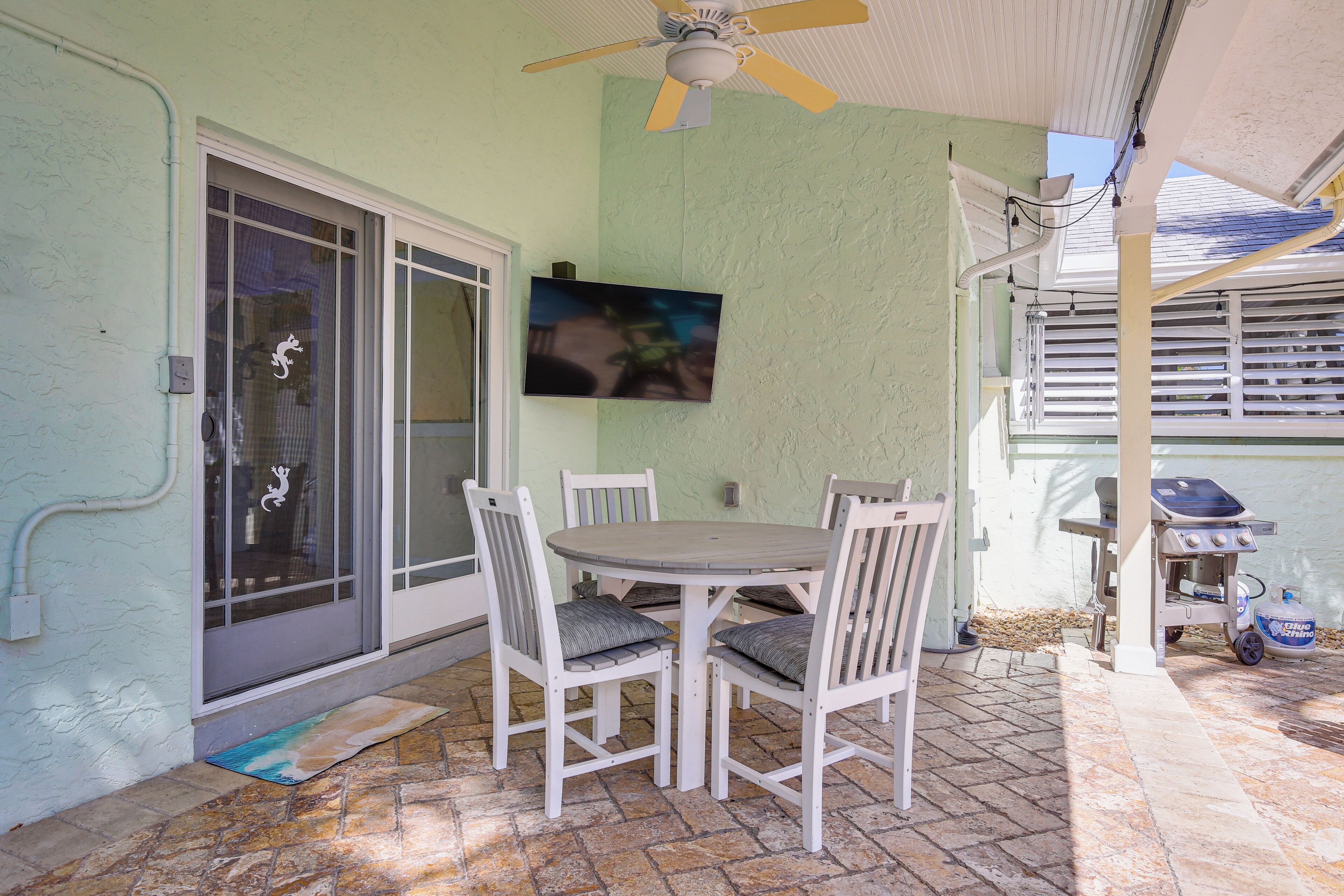 Une terrasse avec une table et des chaises, un ventilateur de plafond et un barbecue.