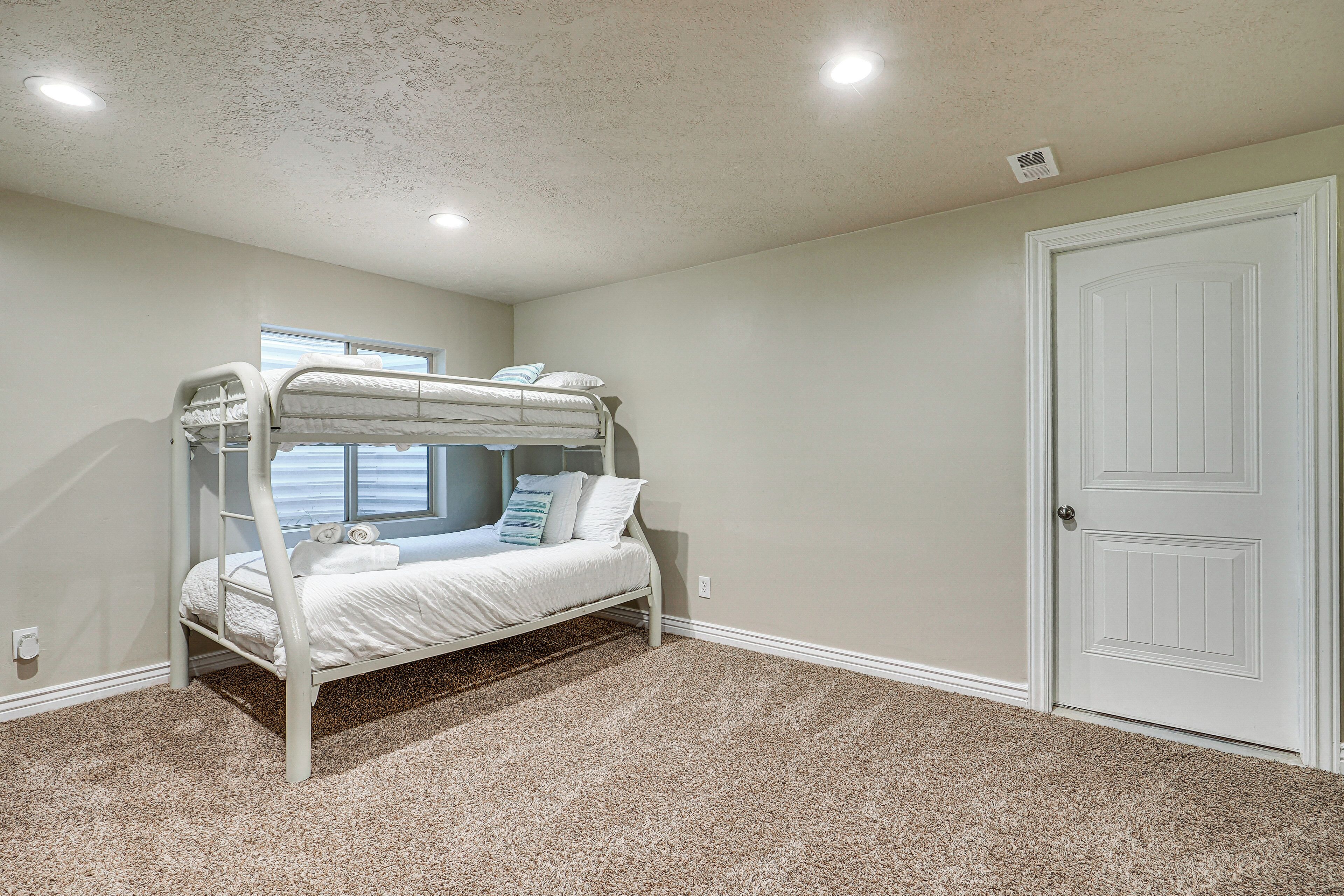 A bunk bed room with a window, carpeted floor, and a white door.