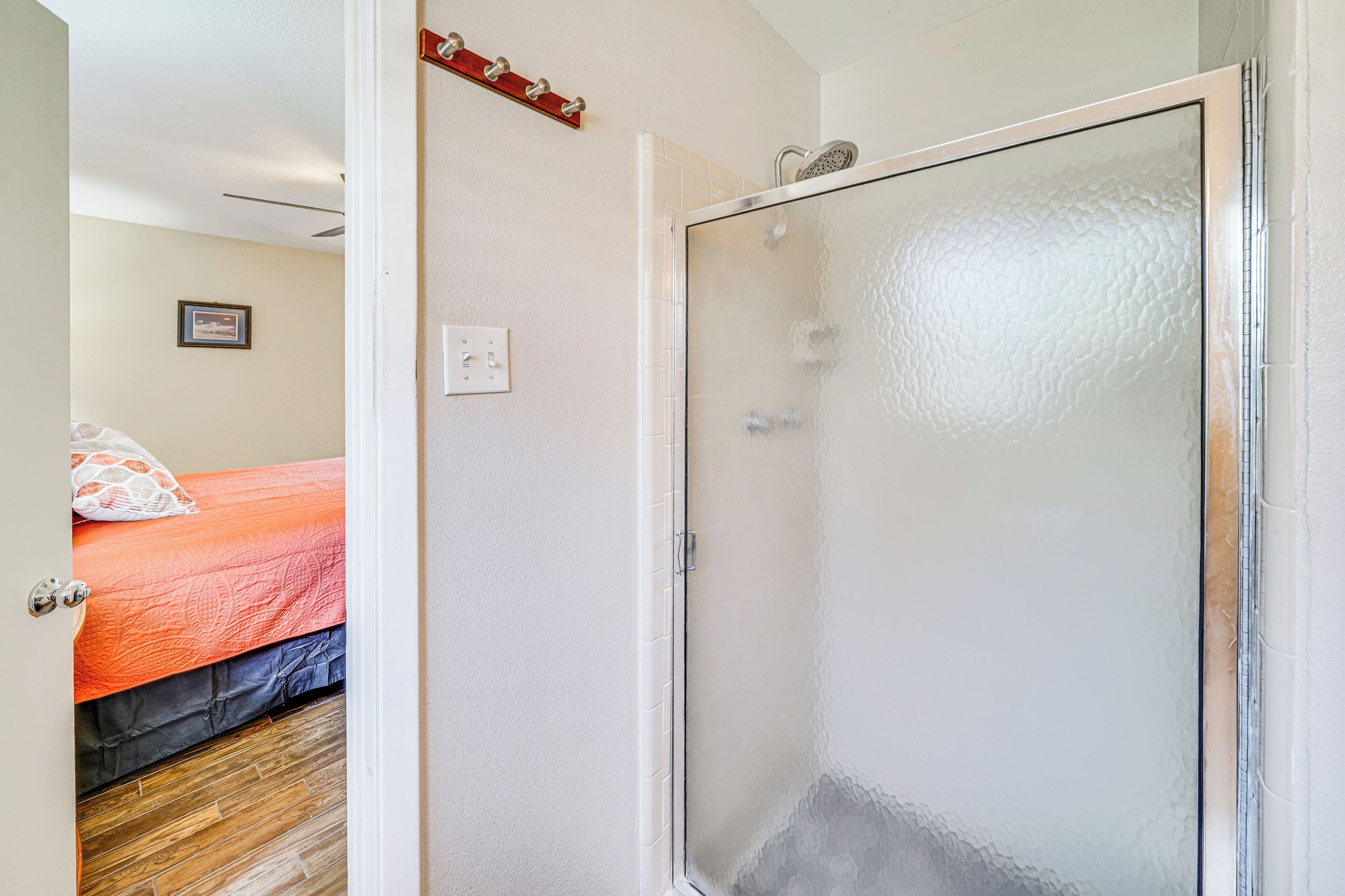 A bathroom with a glass shower door, a white tiled wall, and a wooden floor.