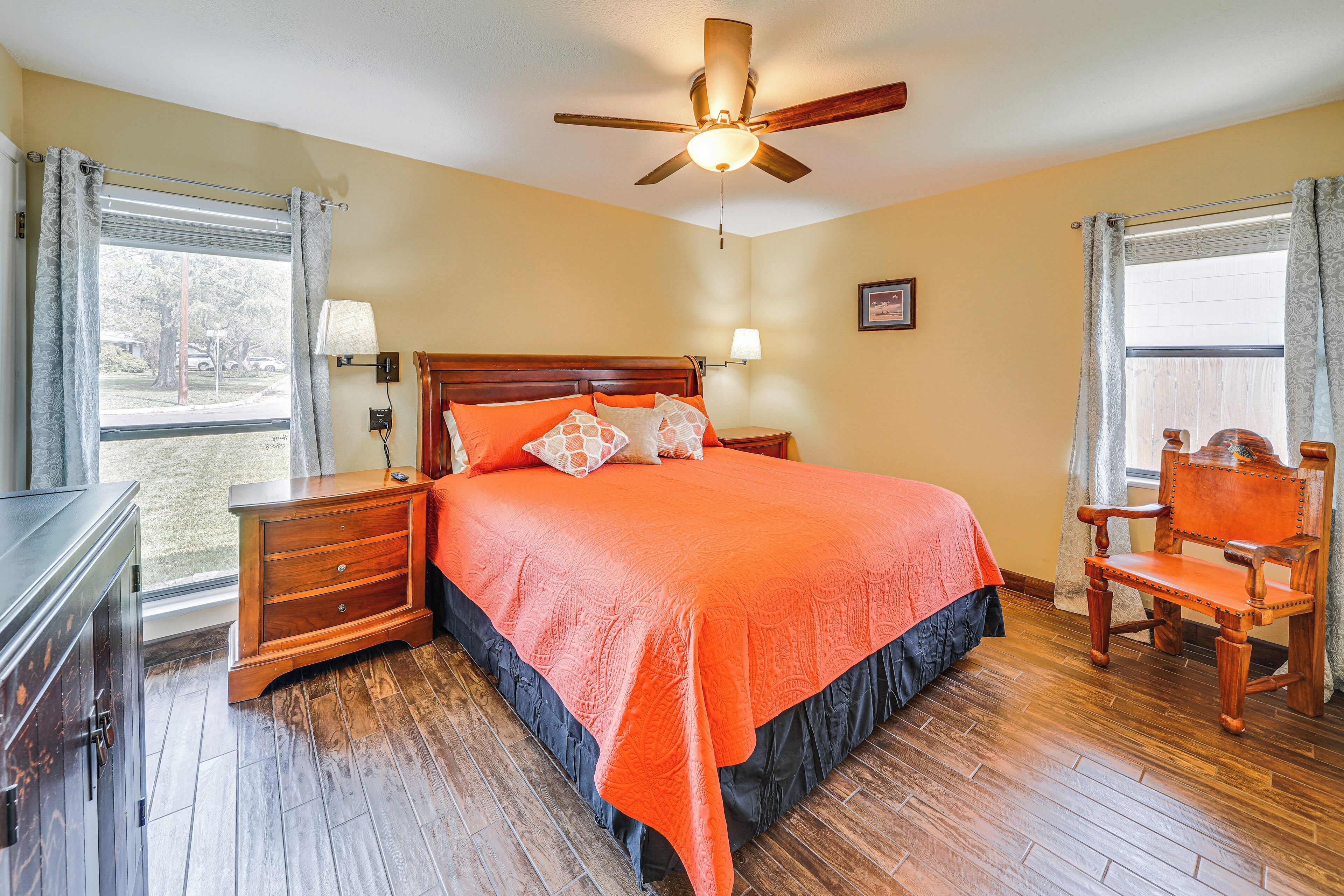 A bedroom with a wooden bed, a nightstand, a chair, a ceiling fan, and a window with curtains.