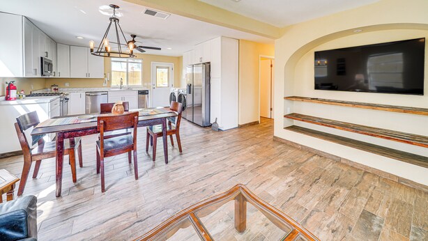 A modern kitchen with white cabinets, a dining area with wooden furniture, and a flat-screen TV mounted on the wall. - Sunny San Antonio Home Near Downtown: Pets Welcome (San Antonio)