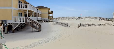 Et hotel ved stranden med en trætrappe til en balkon, en sandstrand i baggrunden og et rødt flag, der angiver et område med begrænsninger.