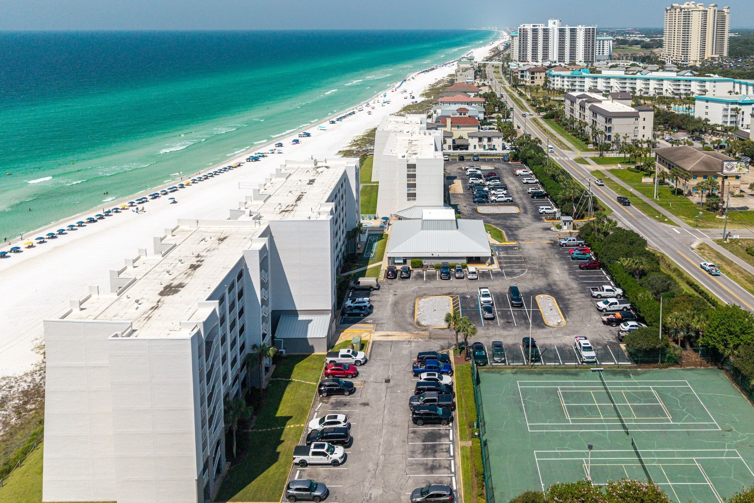 Vista aérea de um hotel à beira-mar, com praia, estacionamento e quadras de tênis.
