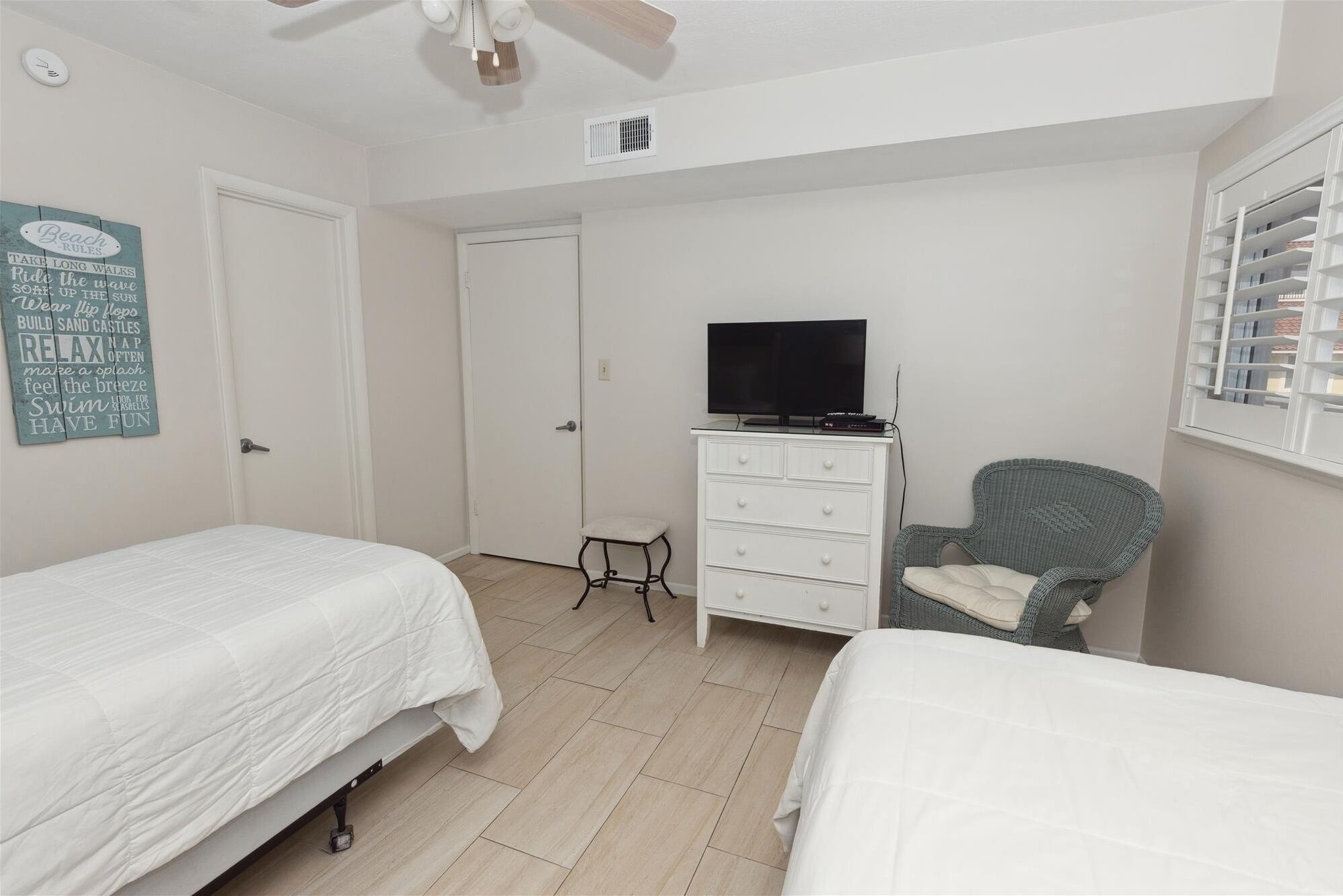 A bedroom with two beds, a TV on a dresser, a chair, and a wall sign.