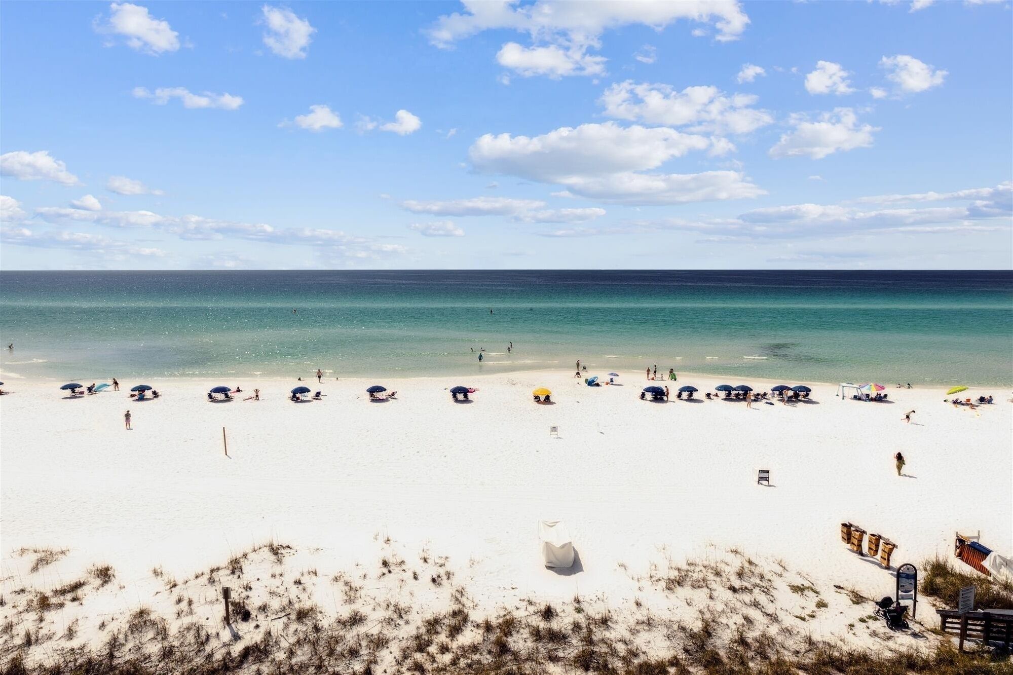Une plage de sable blanc, avec une eau turquoise et limpide, et quelques parasols.
