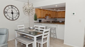 A dining area with a round table, white chairs, and a wall clock.