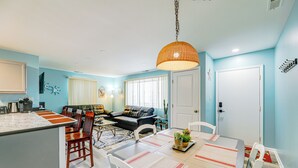 Une cuisine moderne dotée d’un îlot central, un coin repas avec une table et des chaises, et un salon avec un canapé et une table basse.