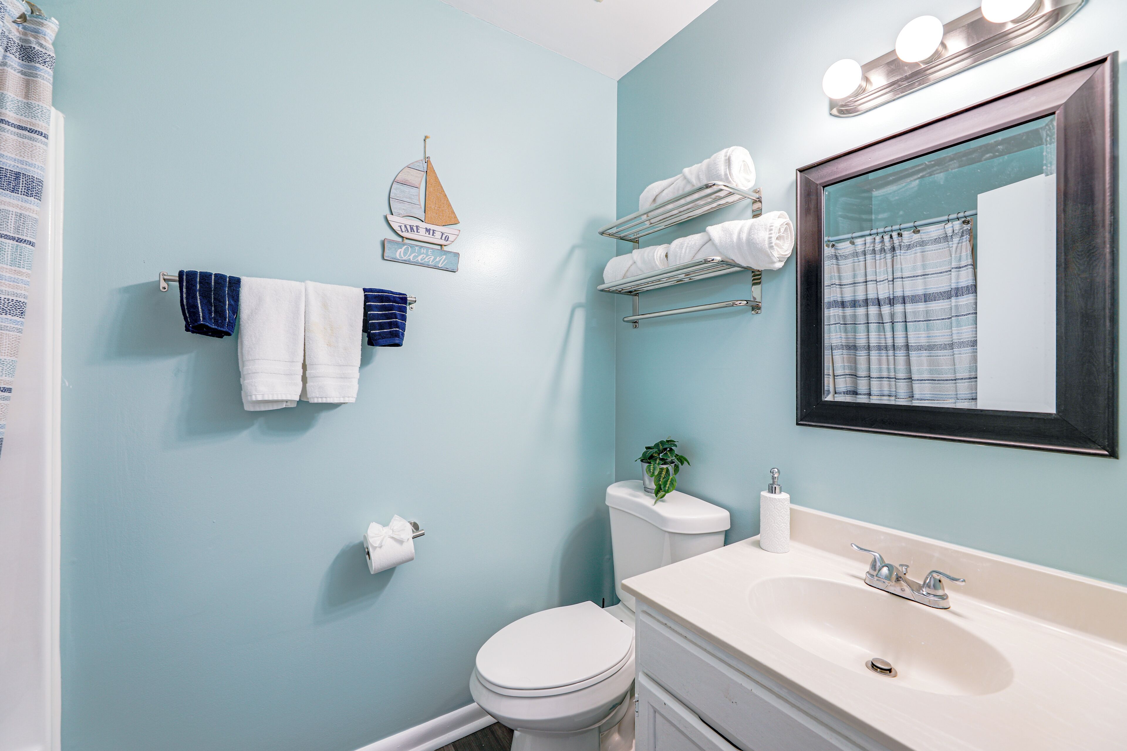 A bathroom with a light blue wall, white fixtures, a sink with a mirror, and a towel rack with folded towels.