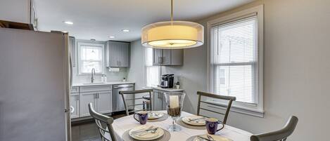 Un coin repas avec une table dressée pour quatre personnes, un lustre et une cuisine en arrière-plan.