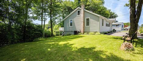 A two-story house with a front yard, a bench, and a tree.