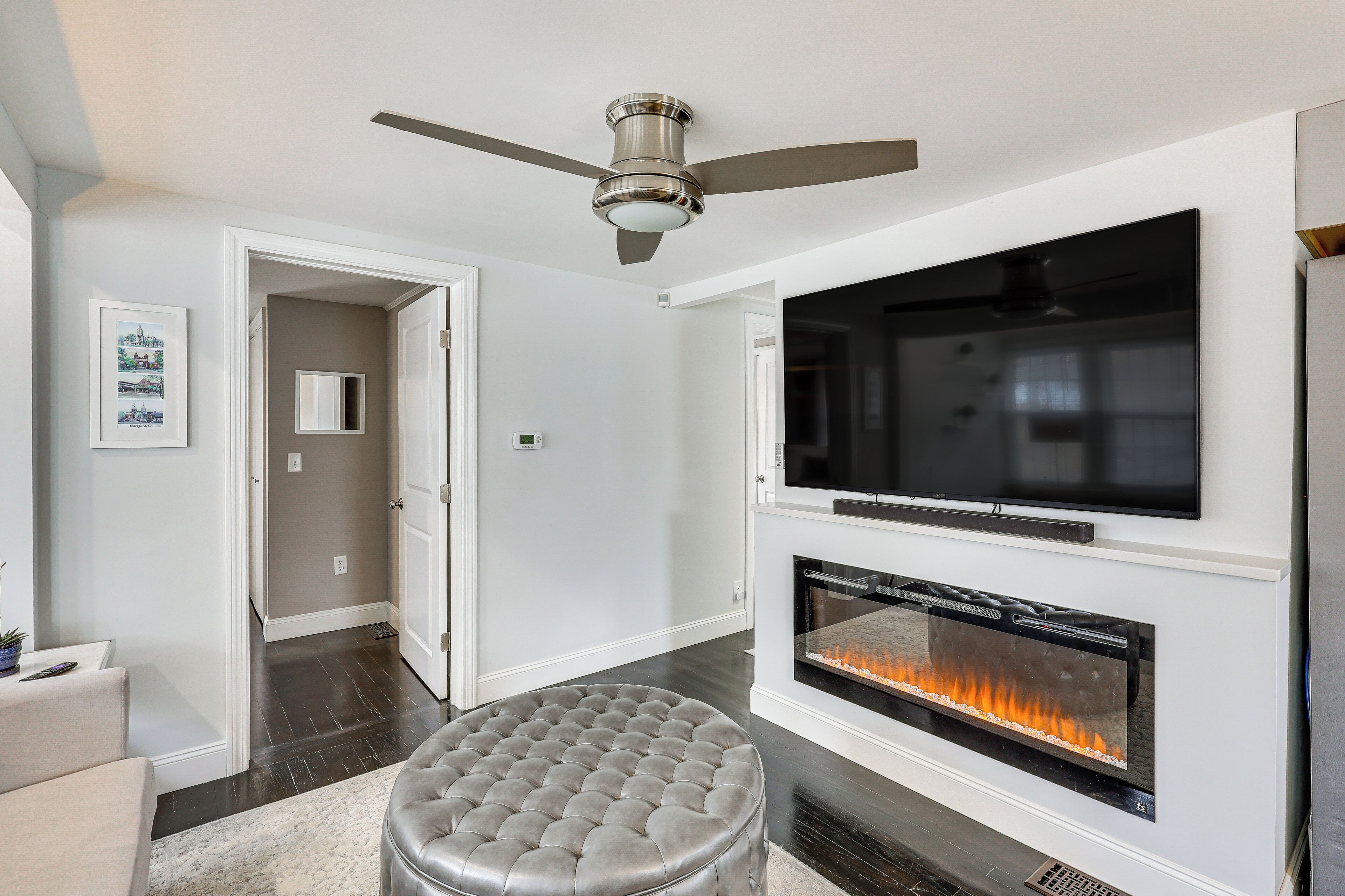 A modern living room with a flat-screen TV, a fireplace, and a ceiling fan.