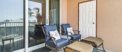 A balcony with two blue chairs, a wooden bench, and a white door.