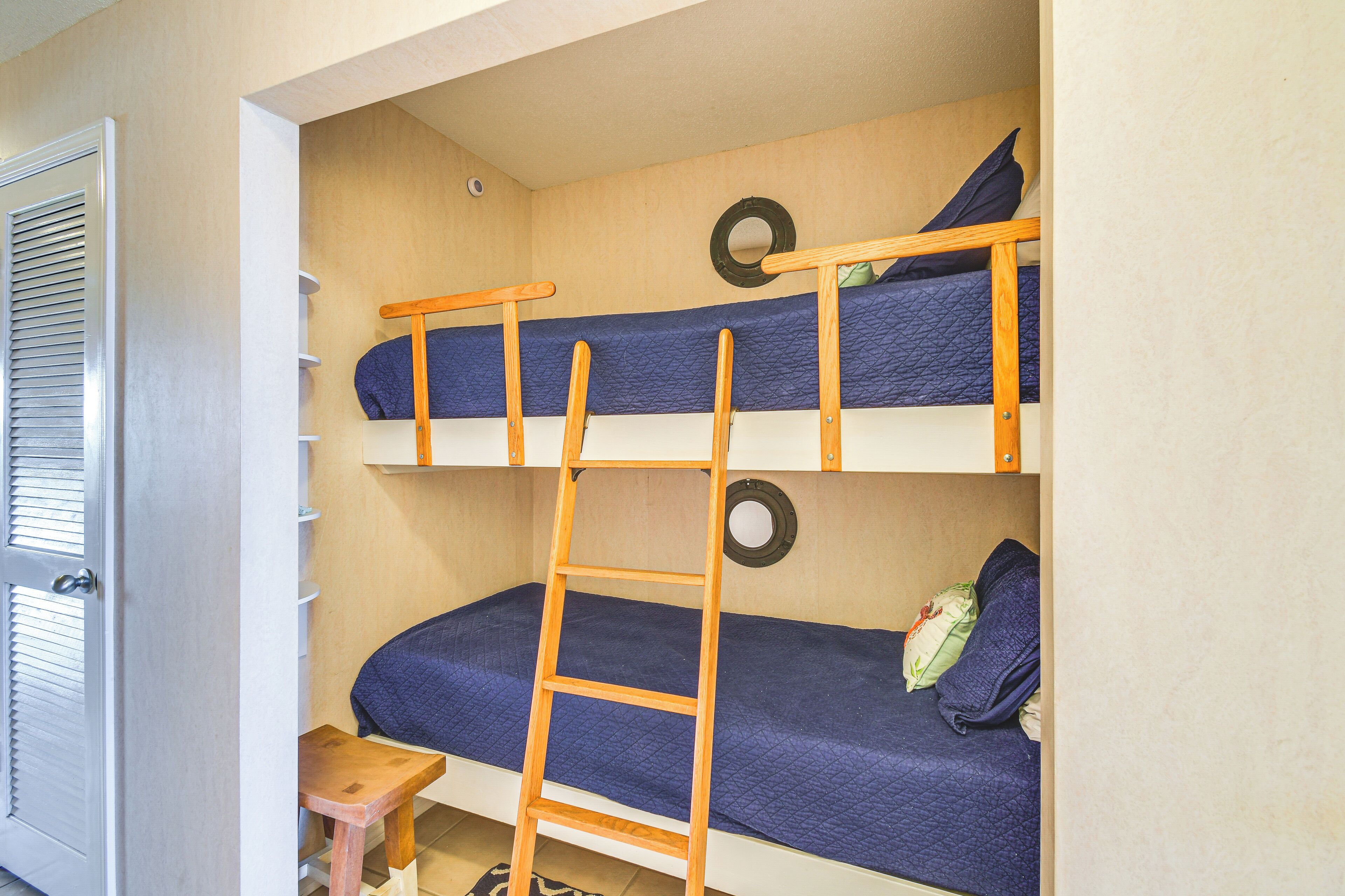 Une chambre avec un lit superposé, une échelle en bois, une petite table et une porte avec des stores.