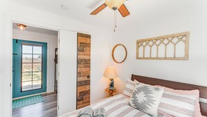 A bedroom with a bed, a wooden door, a window, a ceiling fan, and a wall-mounted light fixture. - Quiet Oasis w/ Hot Tub: 21 Mi to Joshua Tree! (Landers)