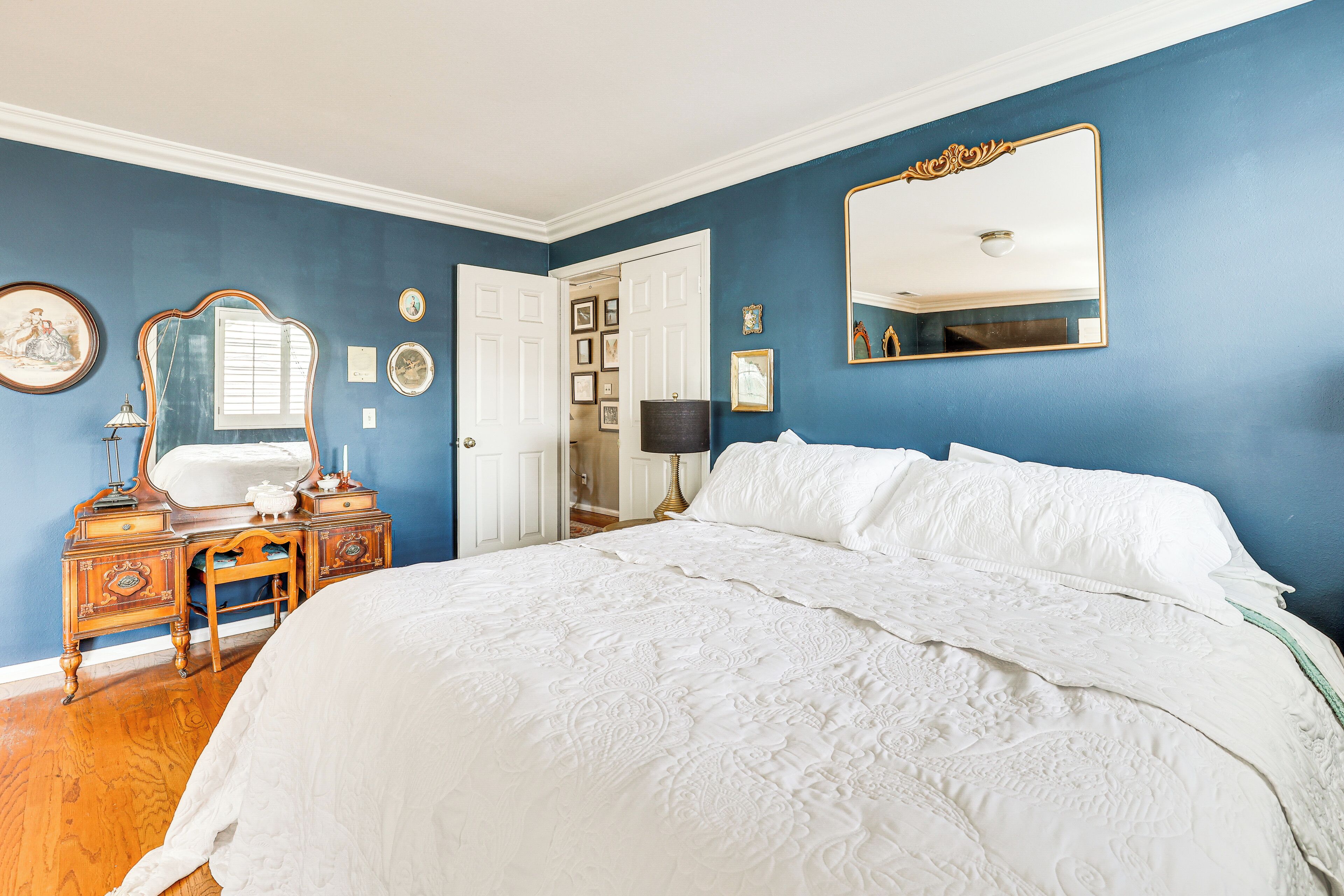 A bedroom with a large bed, a dresser with a mirror, and a door leading to another room.