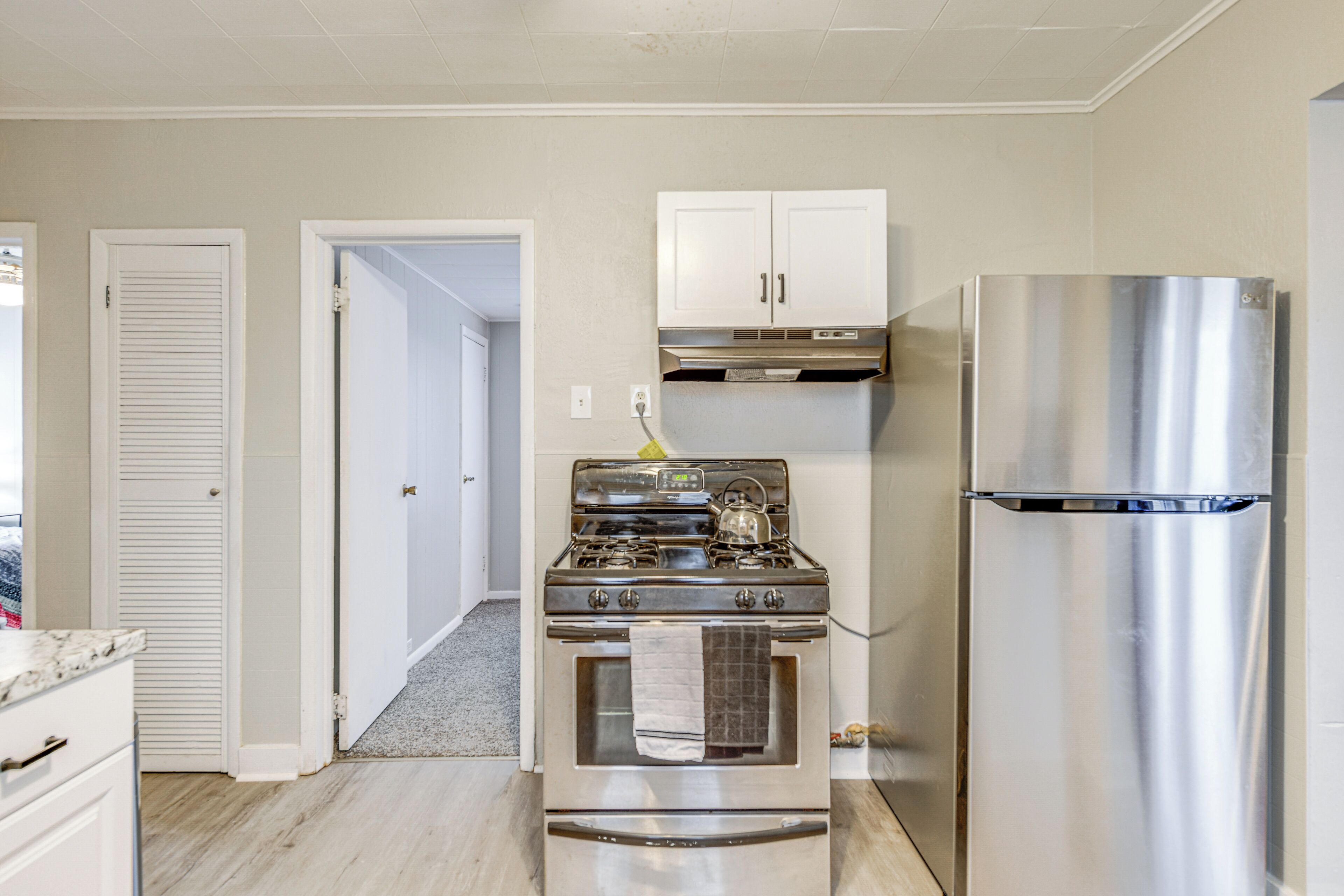 A kitchen with a stainless steel refrigerator, a gas stove, and white cabinets.