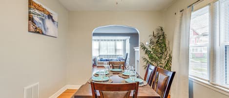 A dining room with a wooden table set for six, a ceiling fan, and a view of the living room through an archway.