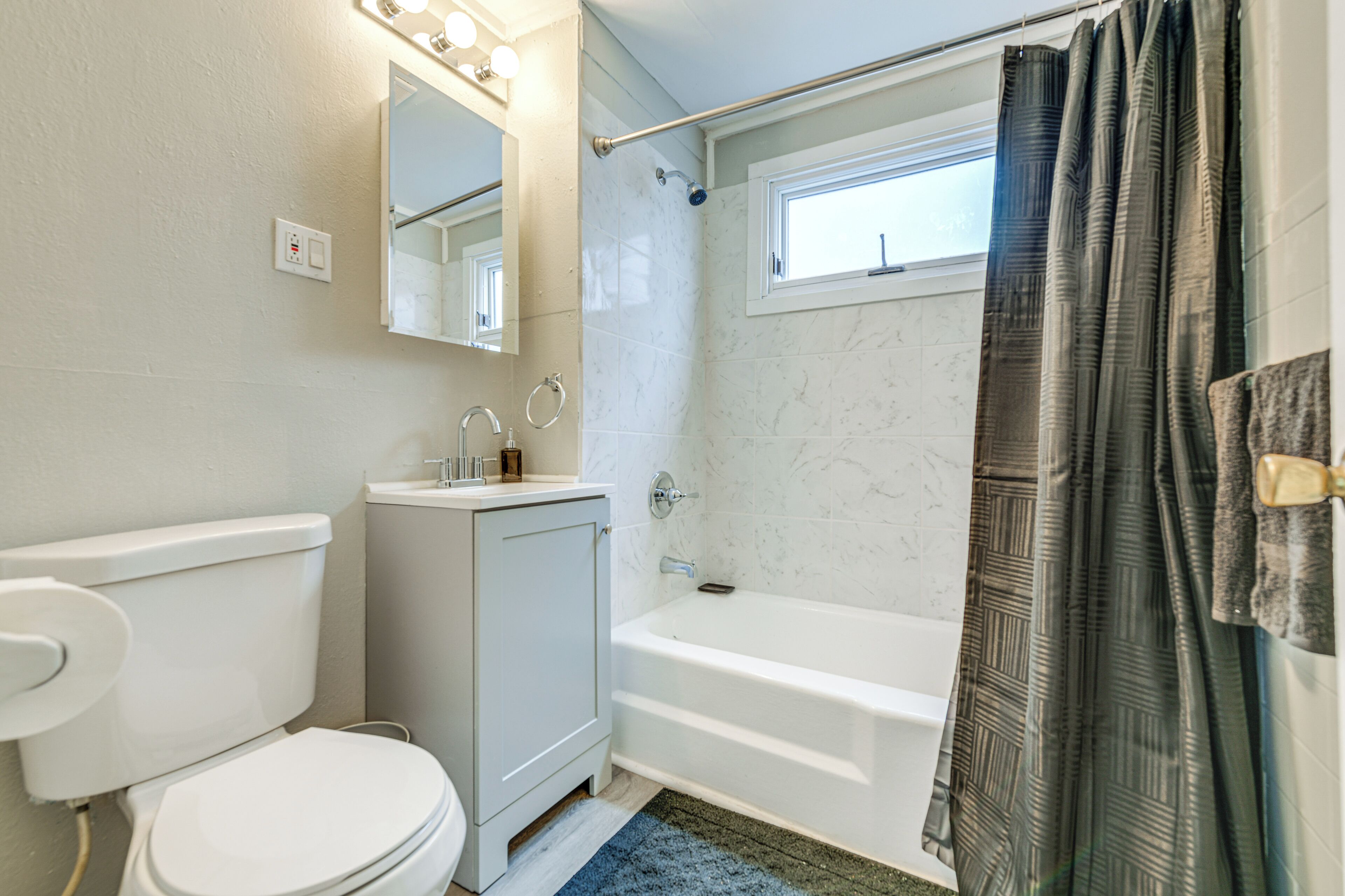 A bathroom with a toilet, sink, mirror, bathtub, and shower curtain.
