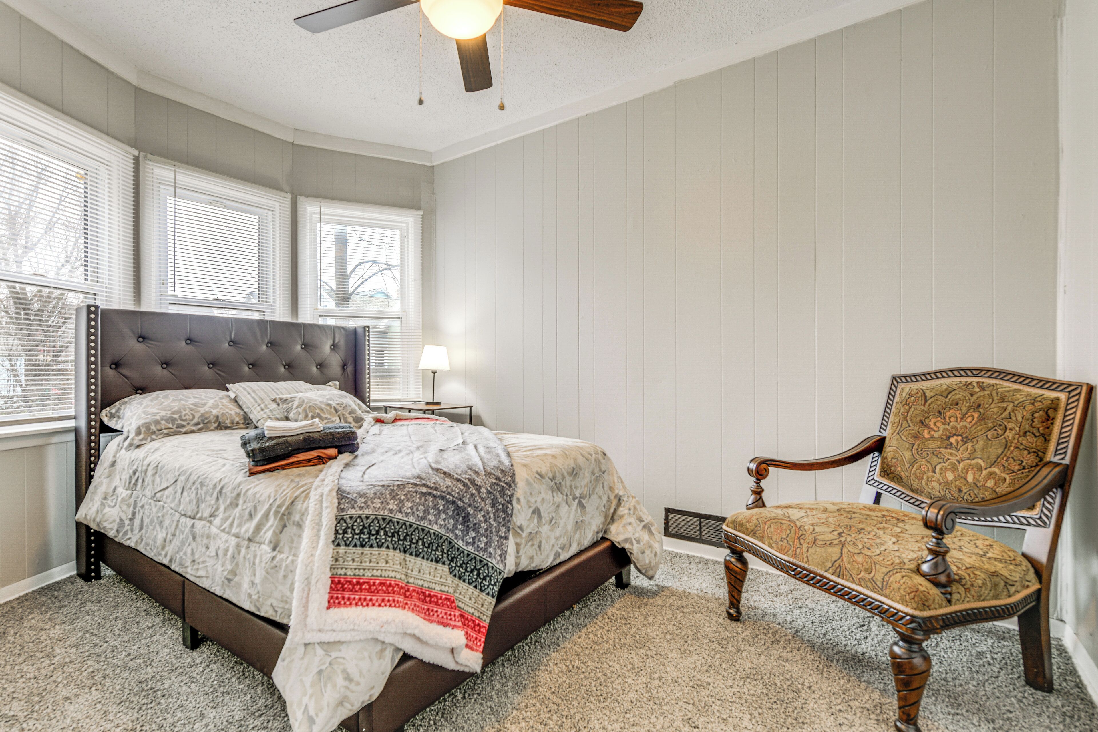A bedroom with a bed, a chair, a ceiling fan, and a window with blinds.