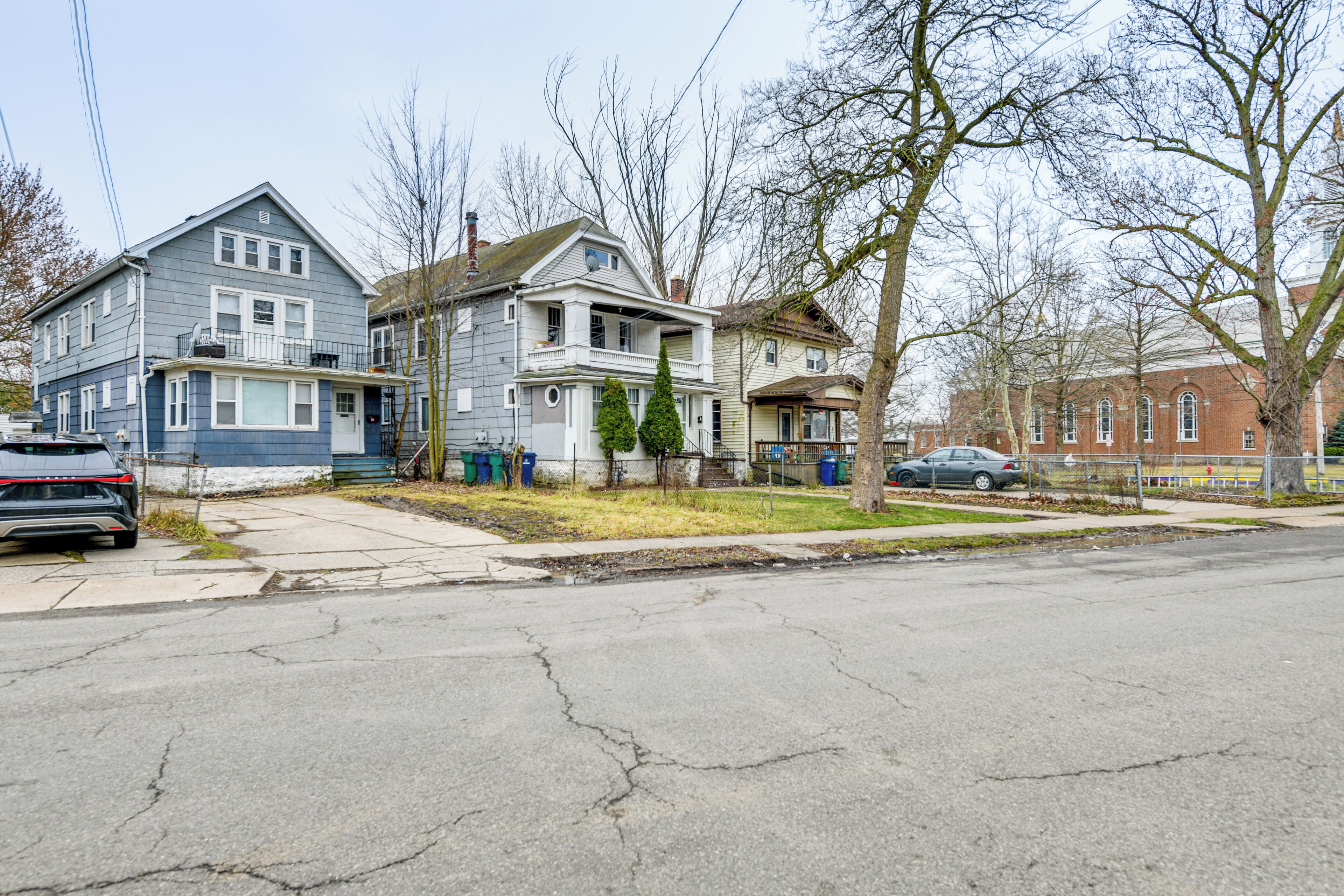 A residential street with houses, a sidewalk, and parked cars.