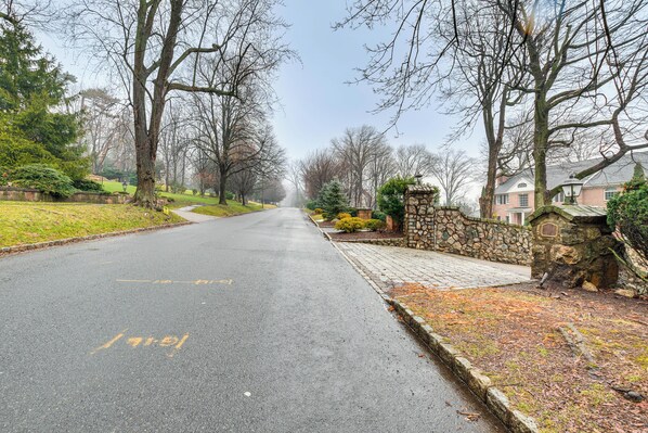 A residential street with a stone wall and a pathway on the right, leading to a house with a stone facade.