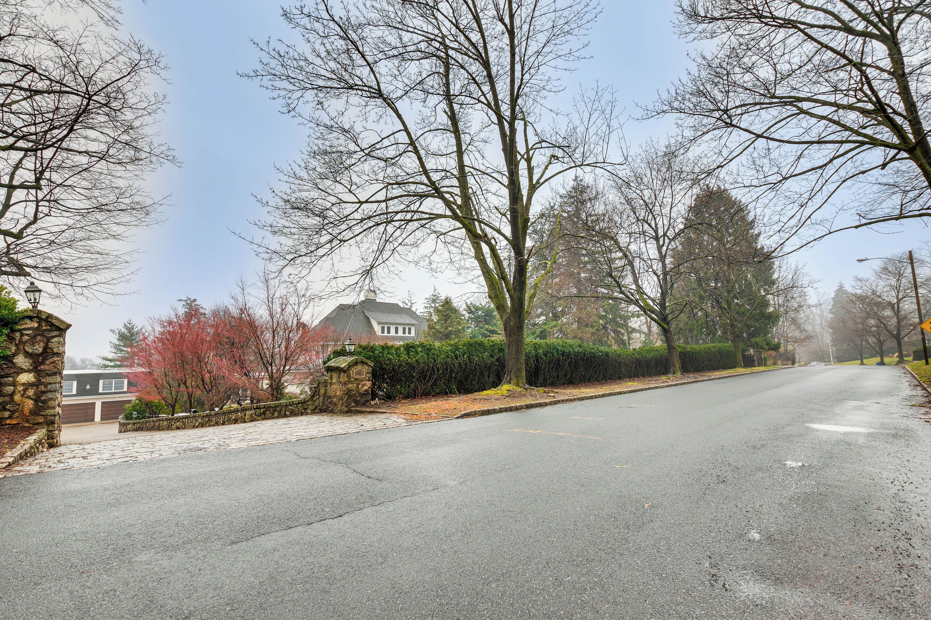 A residential street with a house, trees, and a stone wall.