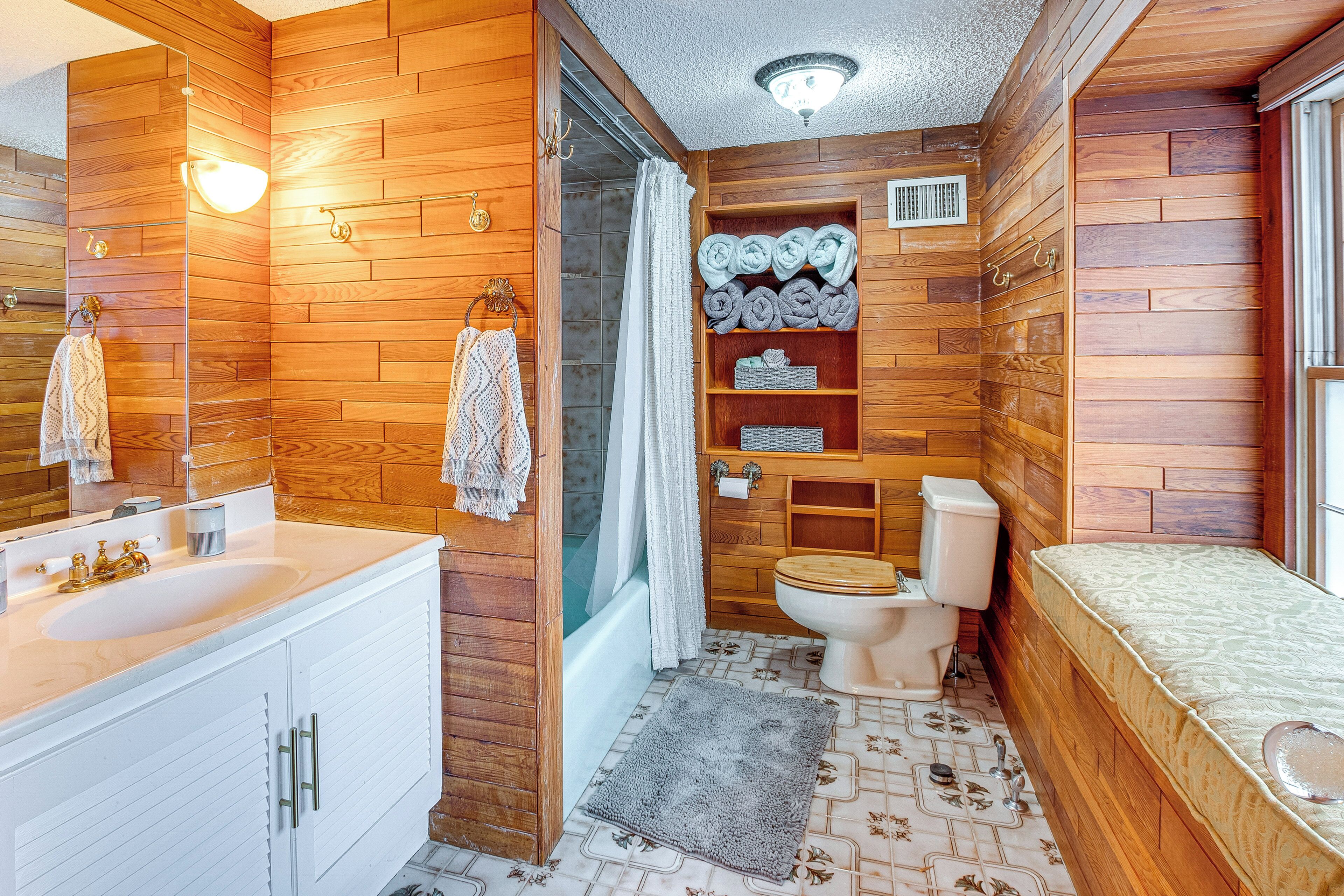 A compact wooden bathroom with a sink, toilet, and shower area.