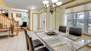 Un espace repas avec une table en marbre, des chaises noires, un lustre et une vue sur les arbres à travers de grandes fenêtres.