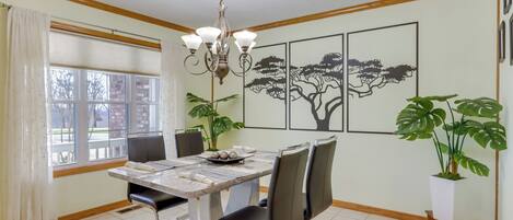 A dining area with a marble table, four chairs, a chandelier, and framed artwork on the wall.