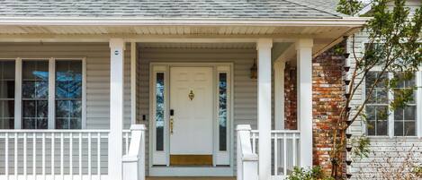 A house with a front porch, a white door, and a brick wall.
