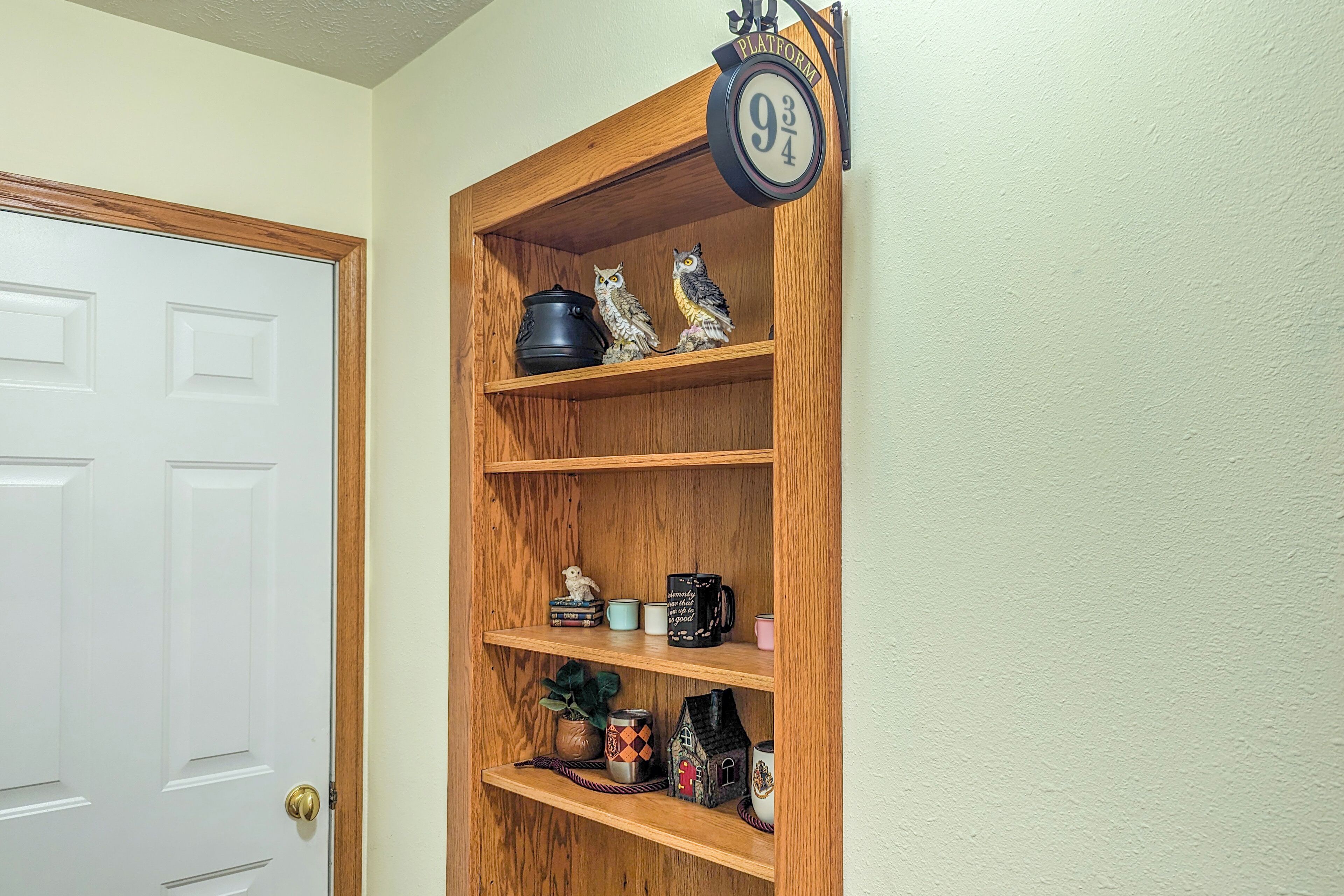 Une étagère en bois sur laquelle sont disposés divers objets, notamment des figurines, des tasses et une petite maquette de maison.
