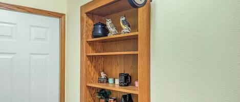 Une étagère en bois sur laquelle sont disposés divers objets, notamment des figurines, des tasses et une petite maquette de maison.