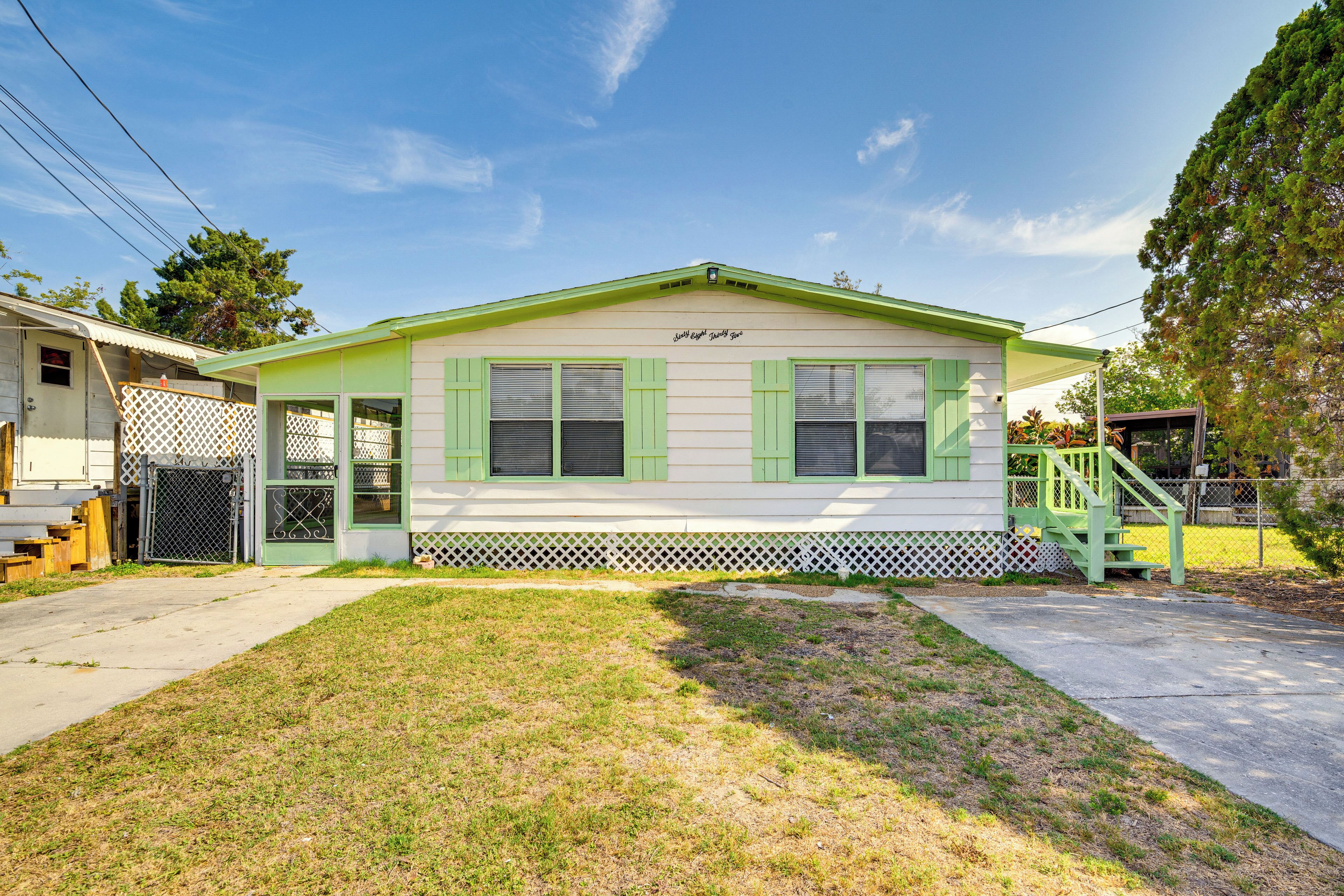 A single-story house with a green roof, white siding, and green shutters. There is a covered porch with a green staircase leading to the front door.
