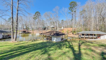 Enjoy serene lakeside views from the property's well-maintained lawn, surrounded by tall trees and featuring a dock for relaxation or recreation.