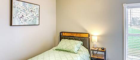 Quarto com cama, mesa de cabeceira, luminária e janela com persianas.