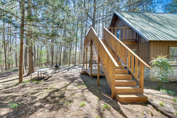 A cabin with a wooden staircase leading to a deck, surrounded by trees. - Cabin w/ Private Hot Tub: 2 Mi to Broken Bow Lake! (Broken Bow)