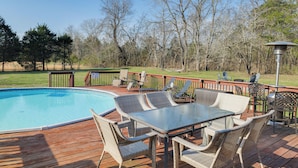 Une piscine avec une terrasse en bois, des meubles en osier et un barbecue.