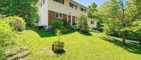 A two-story house with a brick facade and white trim, surrounded by lush greenery and trees.
