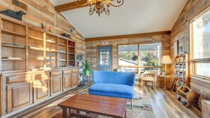 A spacious living room with wooden walls, a blue sofa, a wooden coffee table, and a chandelier. - Creekside Maggie Valley Studio Near Natl Park! (Maggie Valley)
