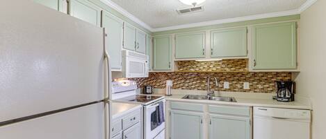 A kitchen with light green cabinets, a white refrigerator, a stove, a sink, and a dishwasher.