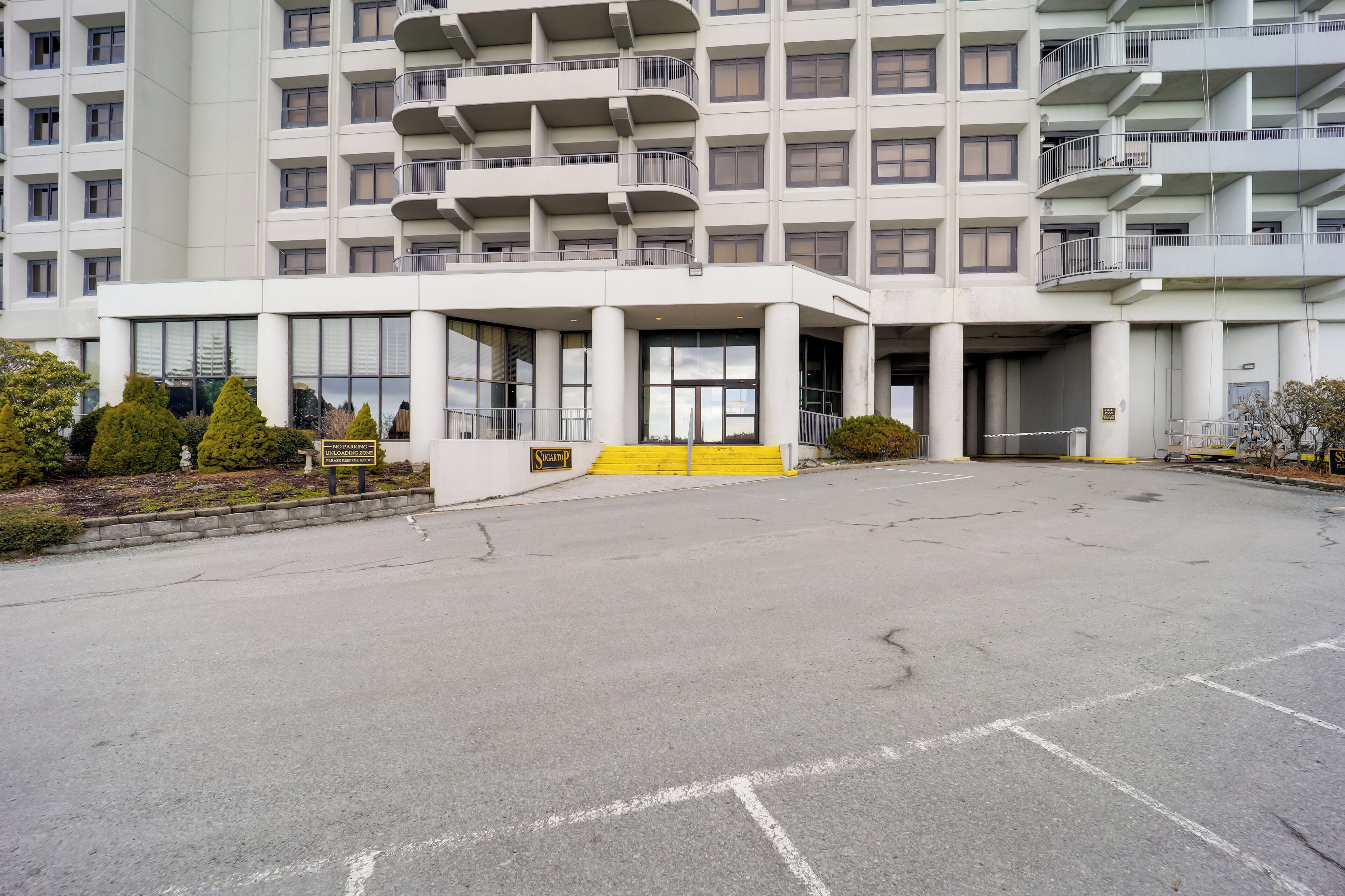 A modern multi-story hotel with a central entrance, large windows, and a parking area.