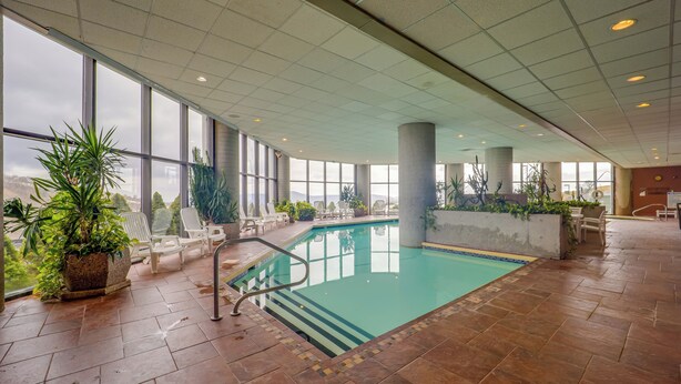 An indoor swimming pool with clear views through large windows, surrounded by potted plants and lounge chairs. - Steps to Slopes! Mtn-view Sugar Top Condo w/ Pool (Banner Elk)