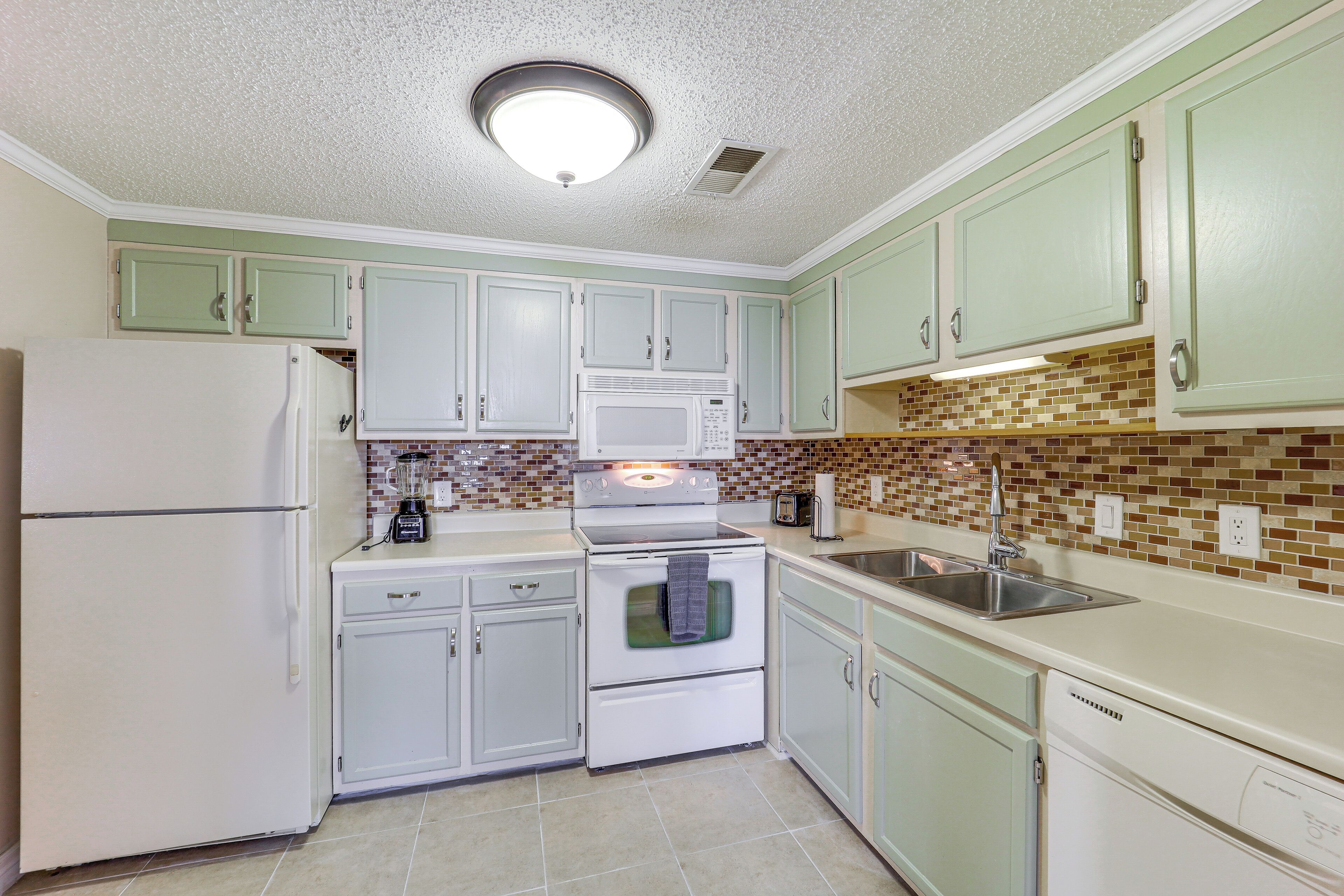 A kitchen with white appliances, green cabinets, and a tiled backsplash.