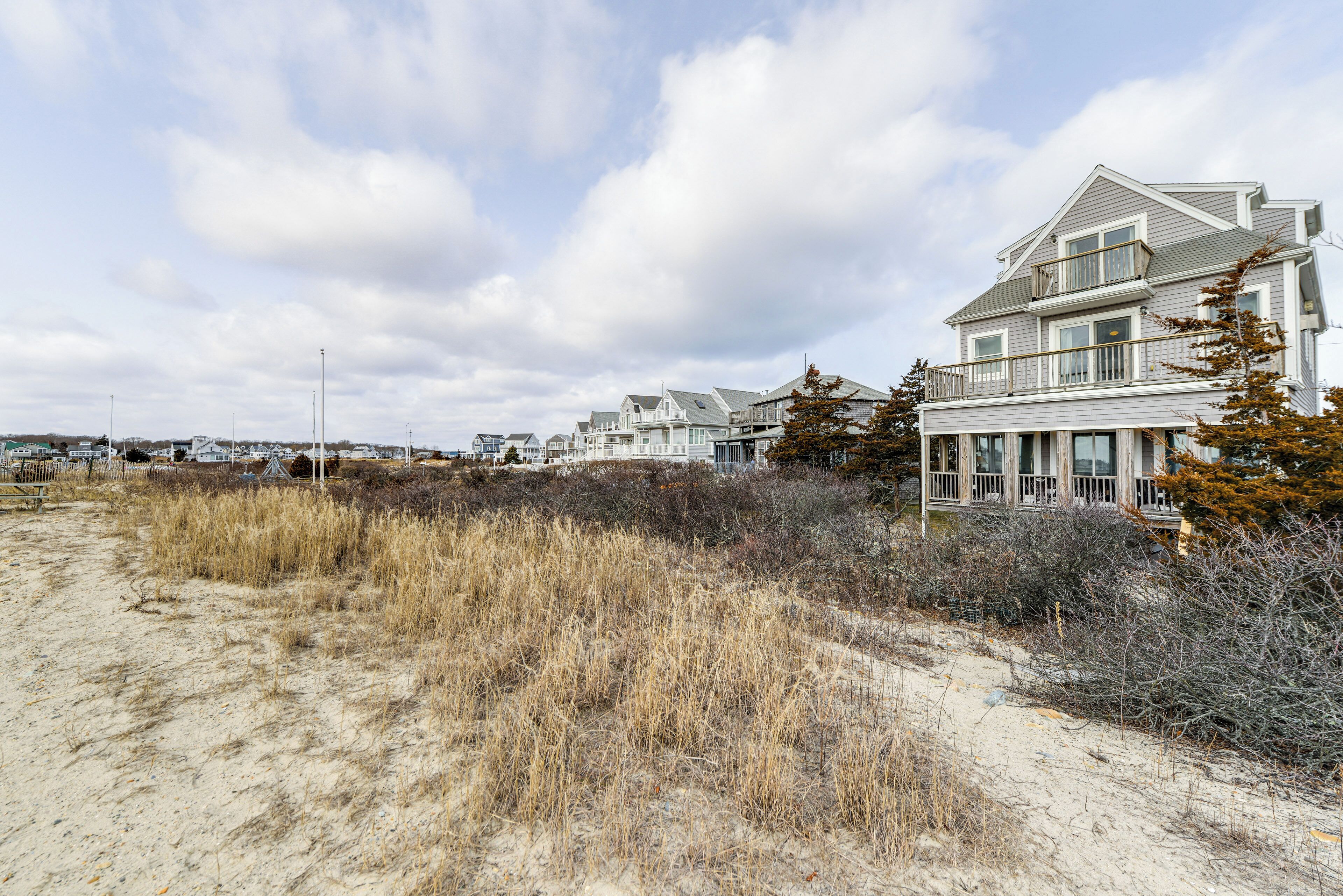 A coastal residential area with houses, sandy beach, and overcast sky.