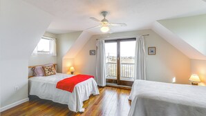 Un dormitorio con dos camas, ventilador de techo, ventana con cortinas y vistas al balcón.