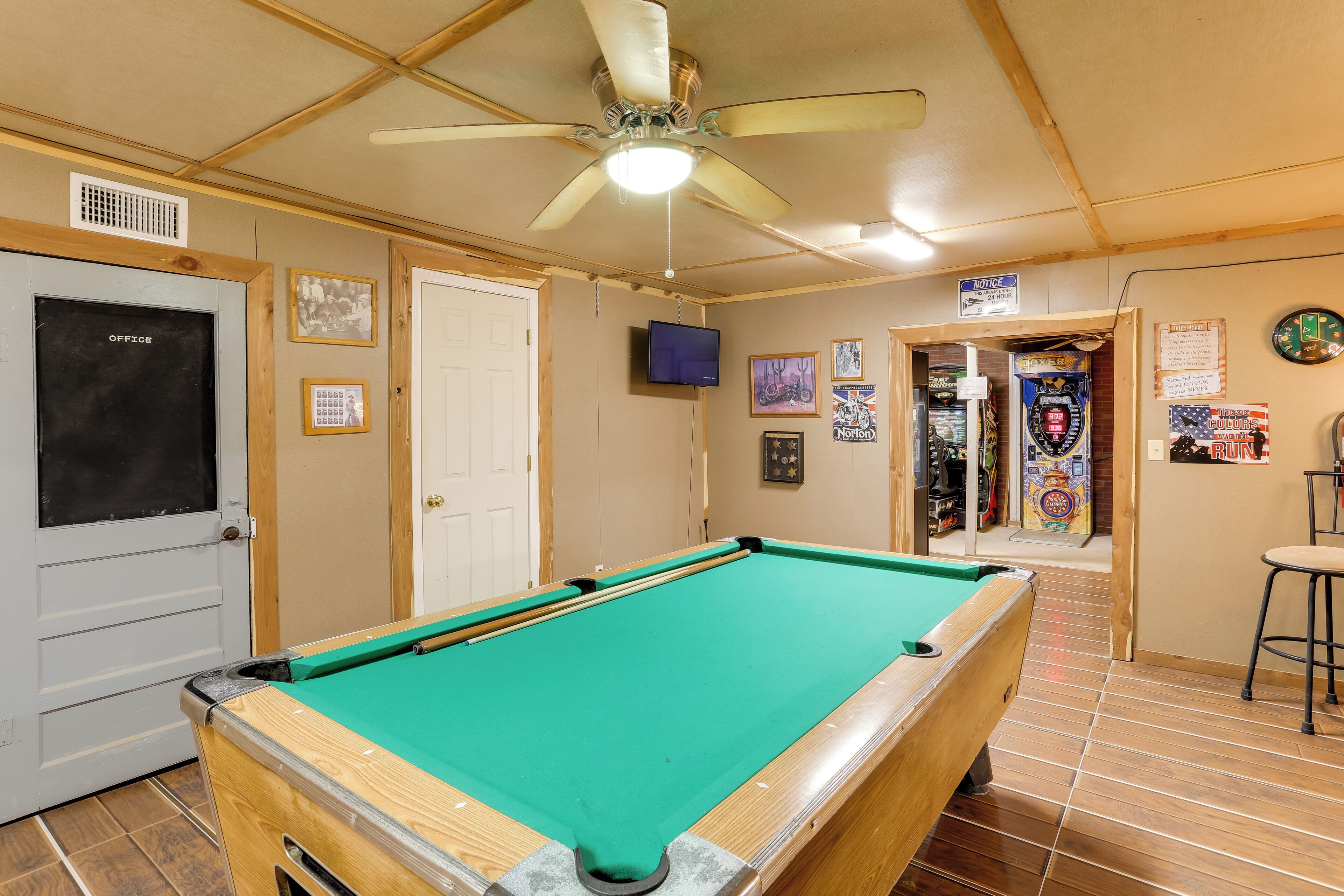 A pool table in a room with wooden walls, a ceiling fan, and various framed pictures.