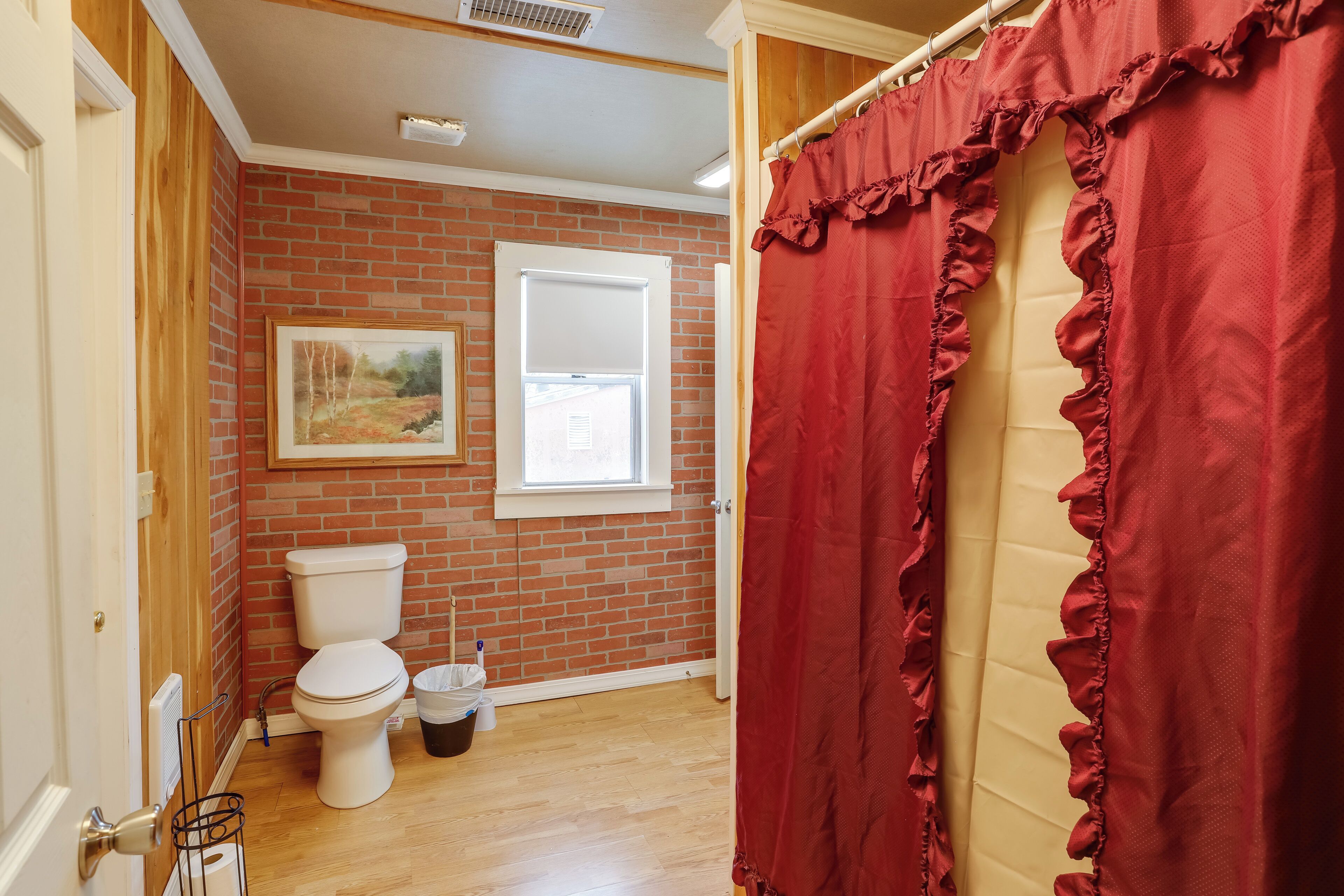 A bathroom with a toilet, a window, and a red curtain.